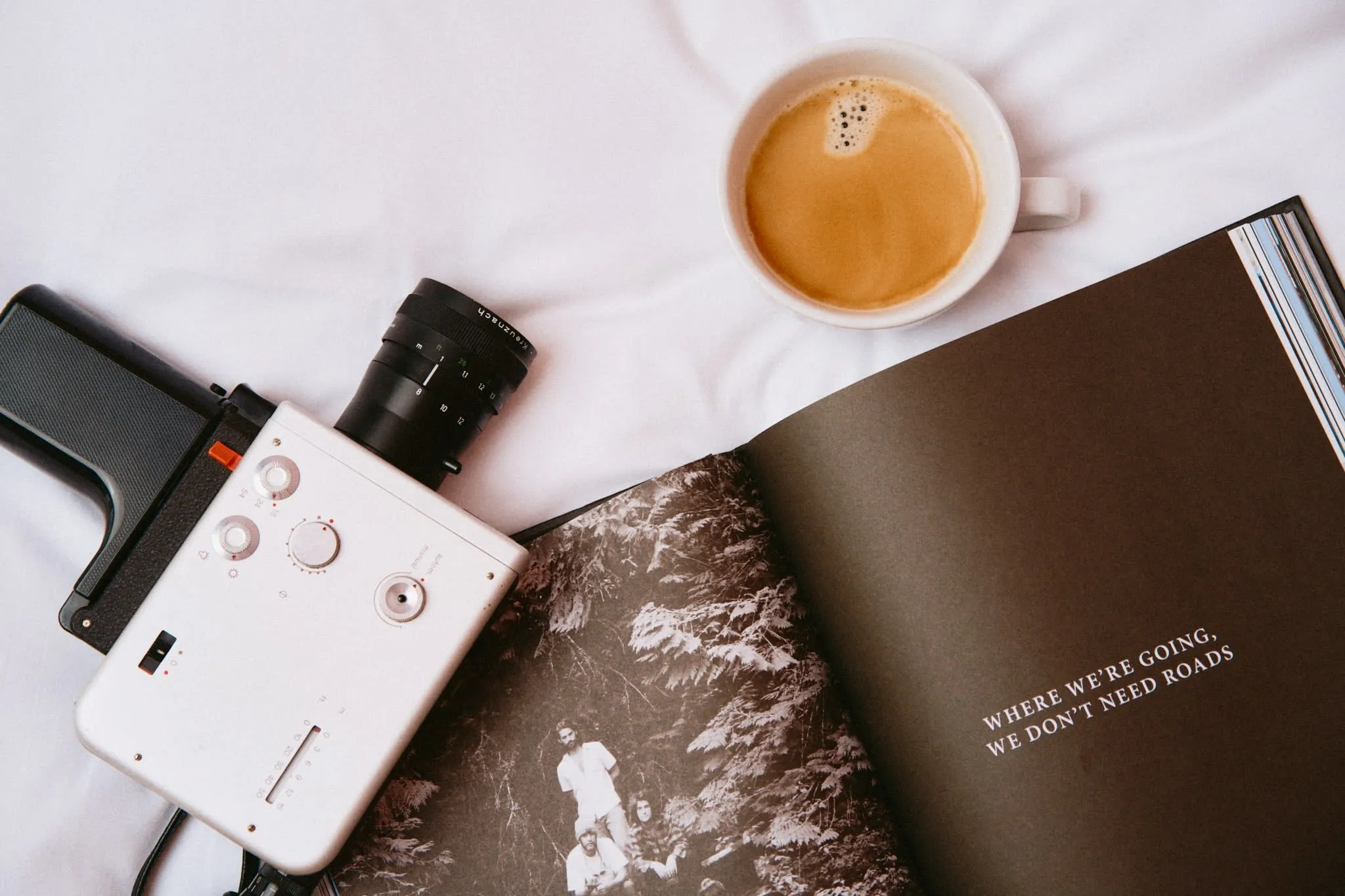 Flat lay of a vintage film camera, an espresso, and an open book with the quote "Where we're going, we don't need roads" — a quiet moment of inspiration and analog nostalgia.